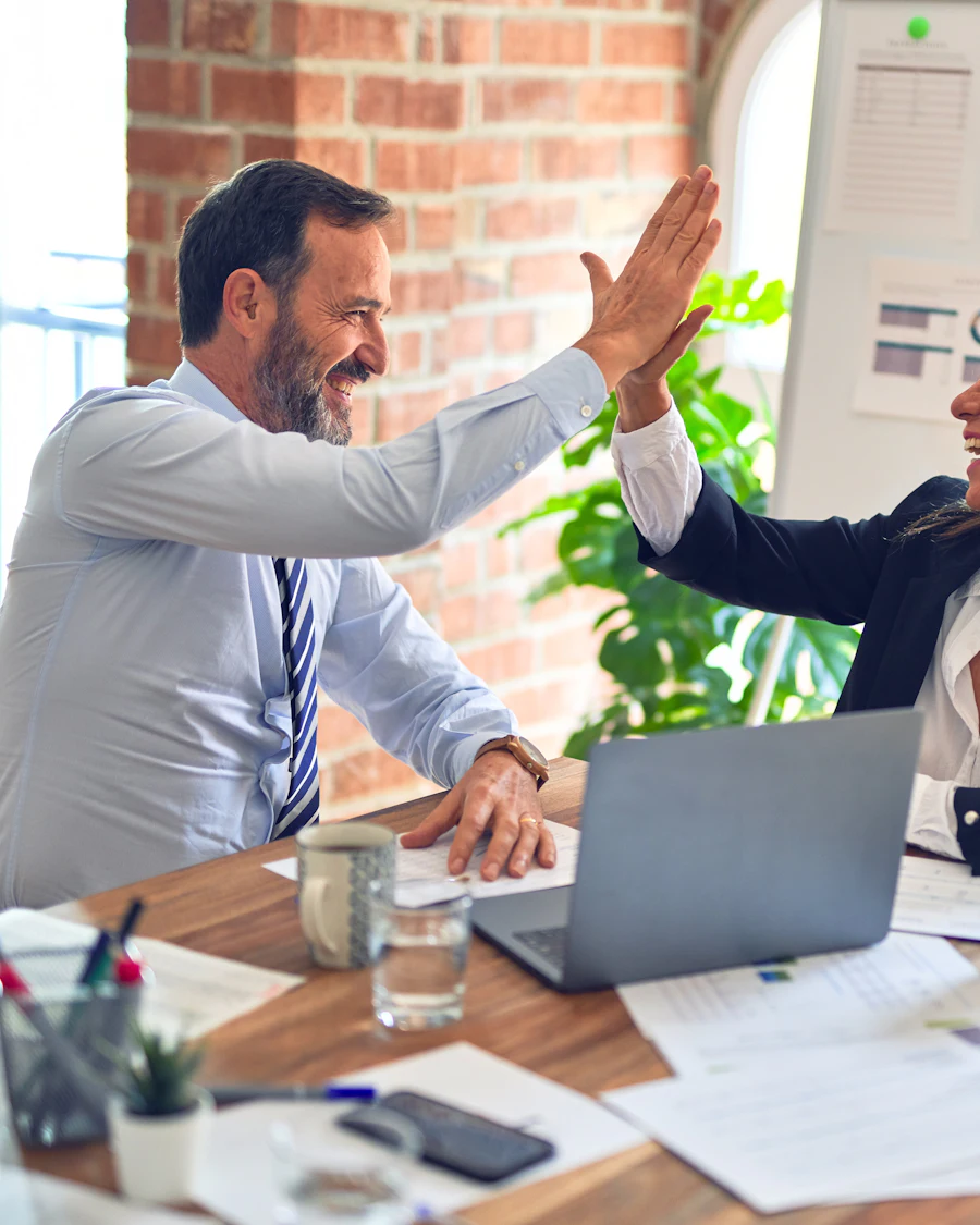 Two professionals celebrating with a high five at an office desk